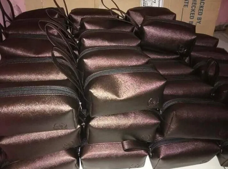 Tumpukan pouch berritsleting berwarna cokelat tua mengilap dengan tali kecil, tersusun rapat di dalam ruang produksi