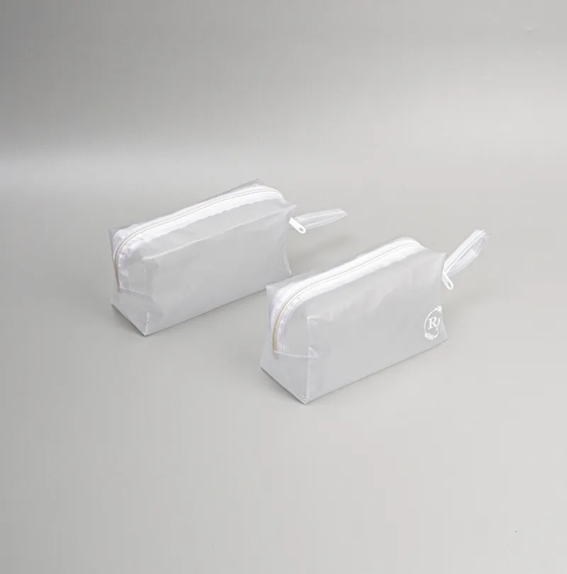 Dua pouch kotak berbahan jelly buram warna putih dengan ritsleting putih dan tali pegangan, di atas alas abu-abu muda