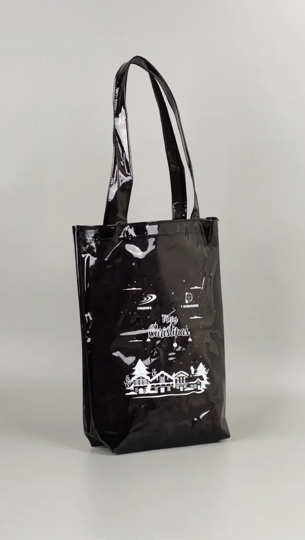 Totebag jelly hitam mengilap dengan dua pegangan hitam dan sablon putih bergambar bangunan serta tulisan ucapan, berdiri di atas alas abu-abu