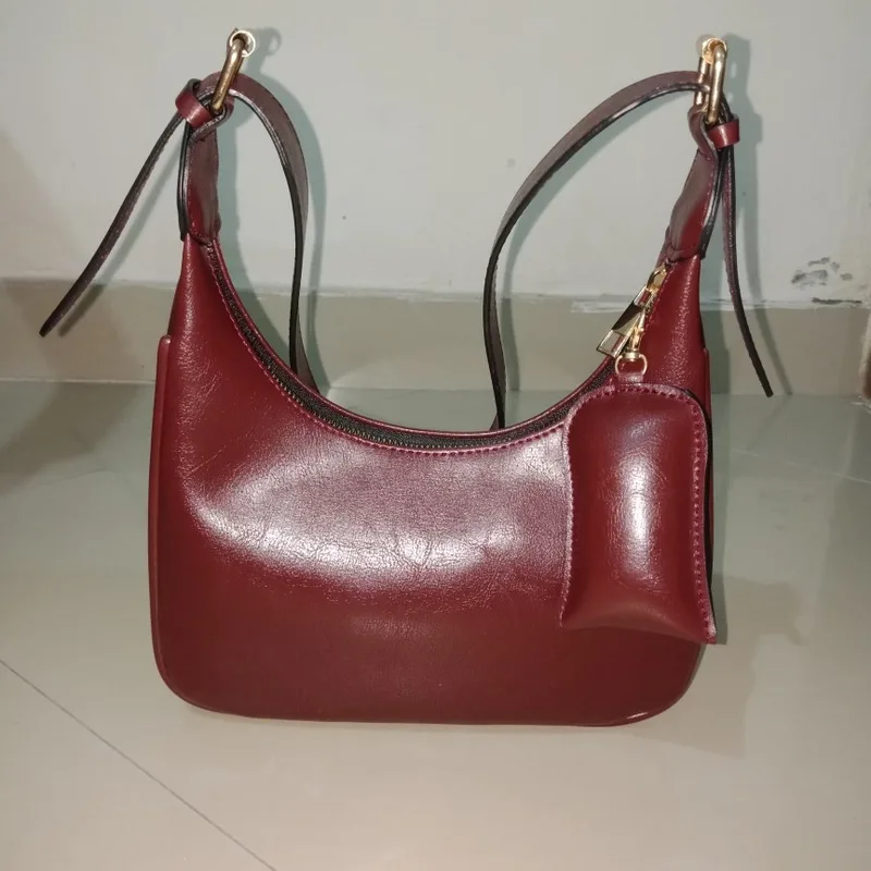 Tas bahu Benita Beela.Co warna merah marun berdiri utuh di atas lantai keramik dengan tali terpasang dan pouch kecil tergantung di sisinya