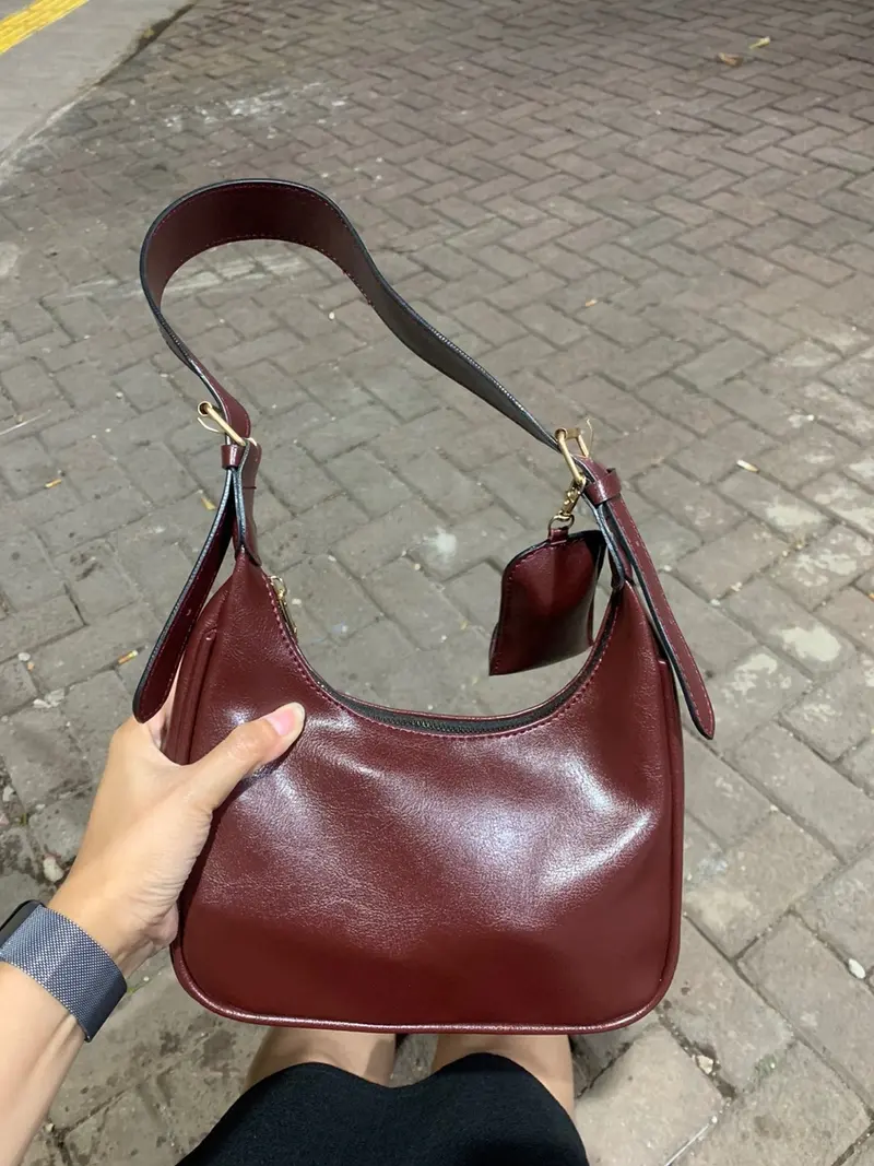 Tas hobo kulit Benita Beela.Co warna maroon dipegang di tangan dengan latar jalan berbatu bata