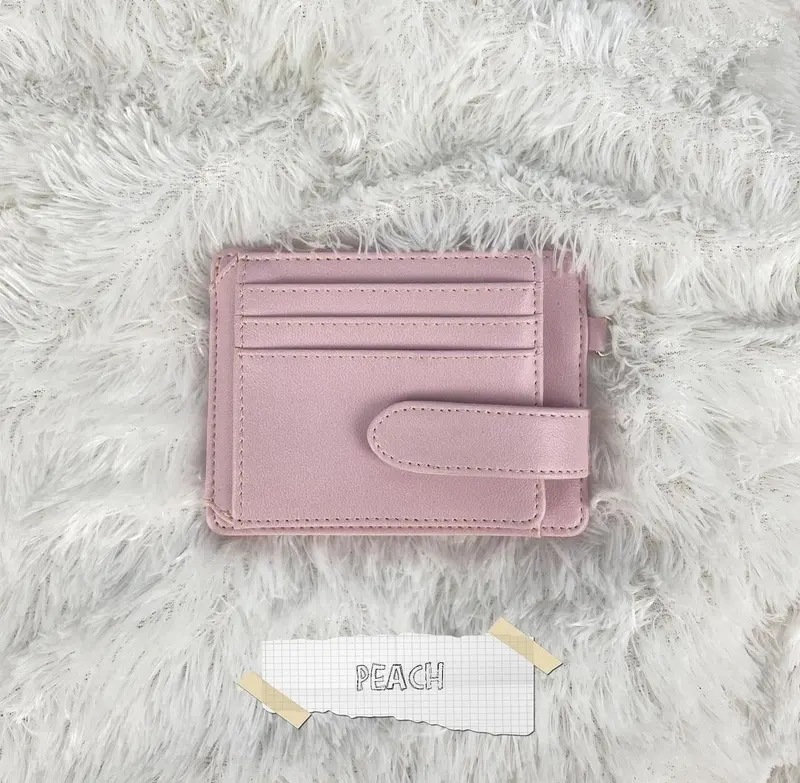 Card holder warna peach dengan slot kartu dan tali berkancing di atas karpet putih dengan label PEACH