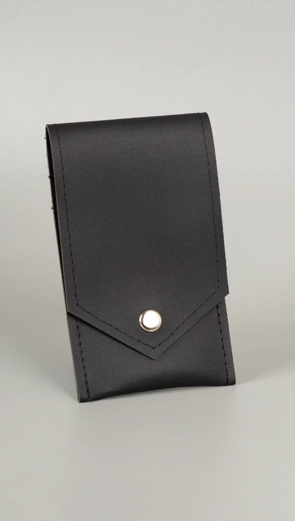 Card holder hitam berbahan vinyl dengan tutup lipat berujung runcing dan kancing logam perak, berdiri tegak di atas latar abu-abu