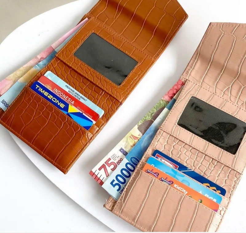 Dua dompet lipat bertekstur croco warna cokelat jingga dan salem dalam keadaan terbuka, berisi kartu di slot, uang kertas di kompartemen uang, dan jendela transparan di panel atas