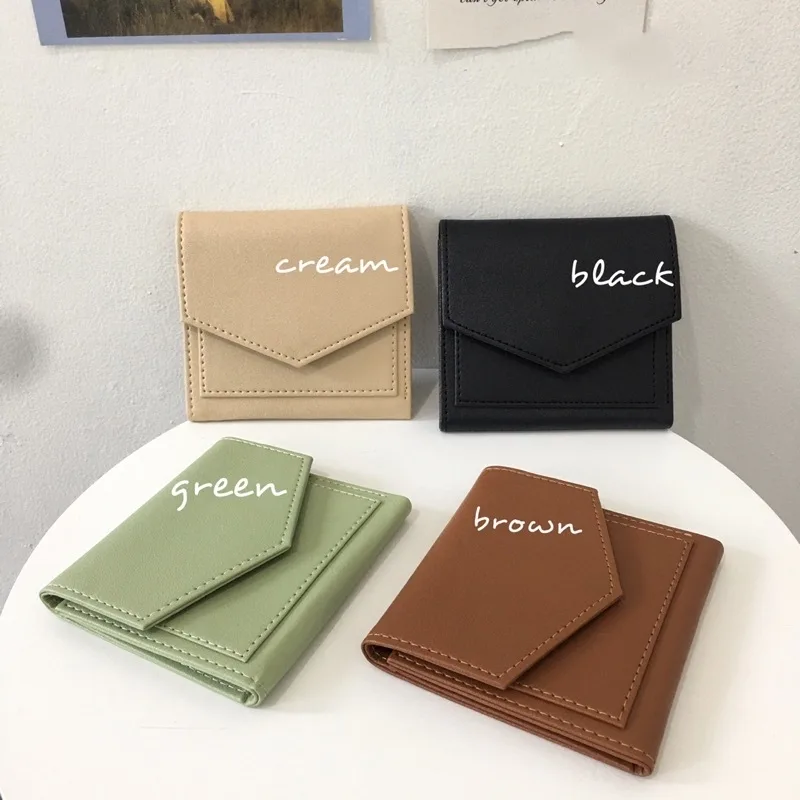 Empat dompet lipat bertutup amplop berwarna krem, hitam, hijau, dan cokelat di atas meja bundar putih, masing-masing diberi label nama warna