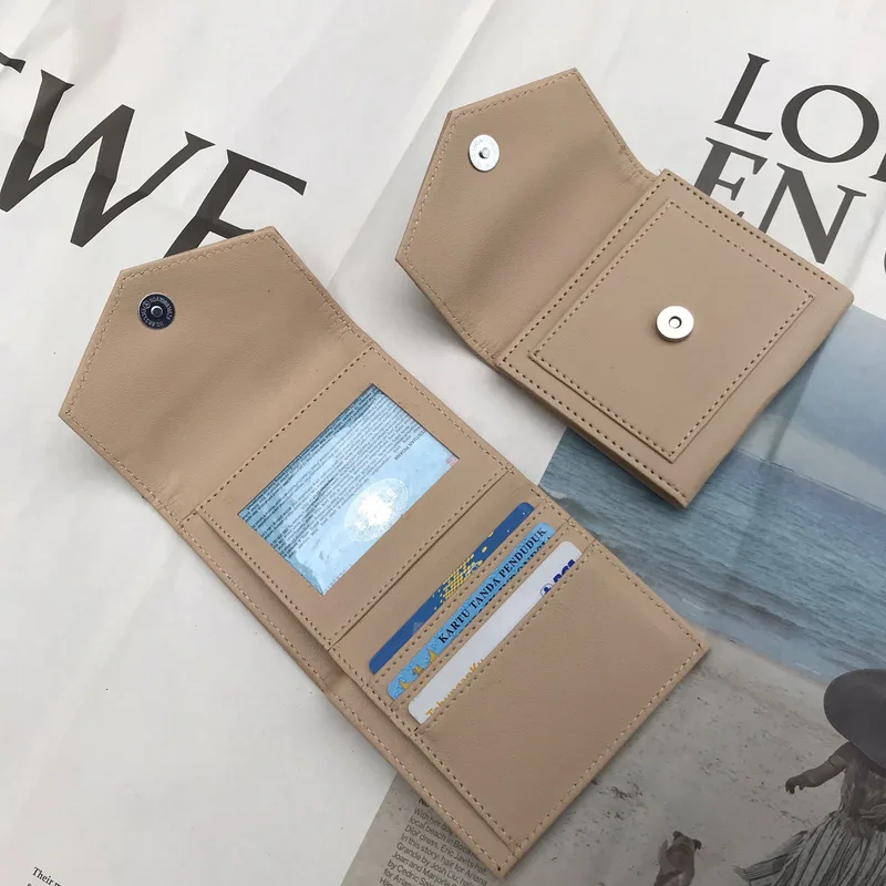 Dua dompet lipat warna krem bertutup amplop dengan kancing magnet, satu terbuka memperlihatkan jendela transparan dan slot berisi kartu, di atas lembaran majalah