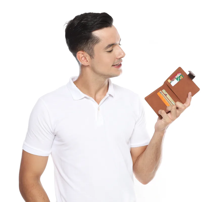 Seorang pria berkaus polo putih membuka dompet lipat berwarna cokelat tan yang berisi beberapa kartu, dengan tali pengunci kecil di sisinya