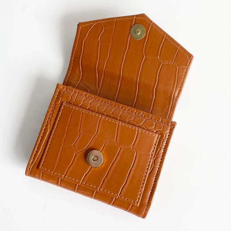 Dompet lipat kecil berwarna cokelat karamel bertekstur motif croco dalam keadaan terbuka, memperlihatkan kantong dalam dengan kancing magnet bulat, di atas latar putih