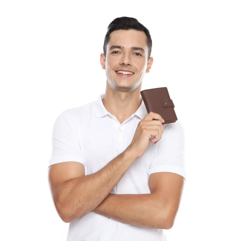 Seorang pria berkaus polo putih tersenyum sambil memegang dompet lipat kecil berwarna cokelat tua dengan tali pengunci berkancing di depan dadanya