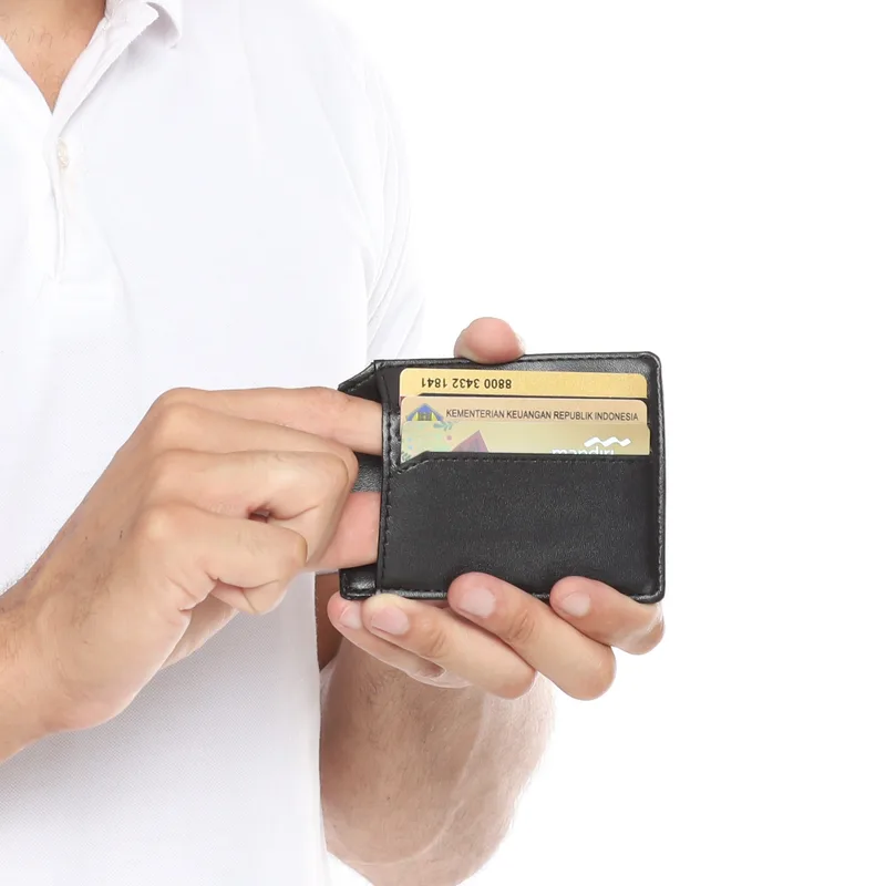 Tangan pria menarik kartu dari slot depan dompet tipis berwarna hitam yang dipegang dengan kedua tangan, dengan jahitan tepi dompet terlihat jelas