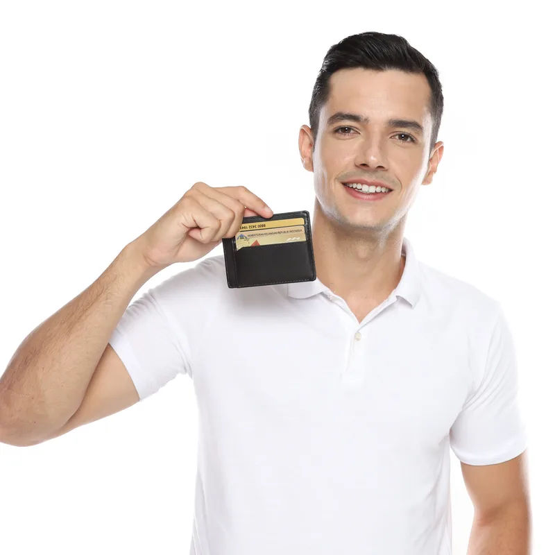 Pria tersenyum mengangkat dompet tipis hitam berisi beberapa kartu di dekat bahu kanannya, berlatar putih polos