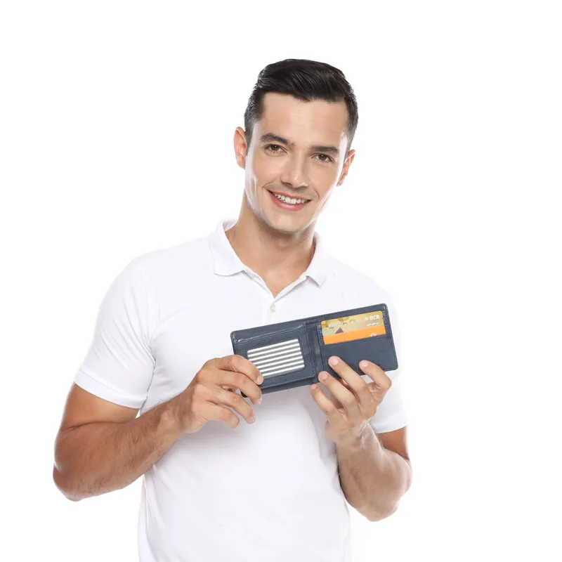 Pria berkaus polo putih tersenyum memegang dompet bifold biru dongker yang terbuka, memperlihatkan jendela kartu identitas dan kartu di slot