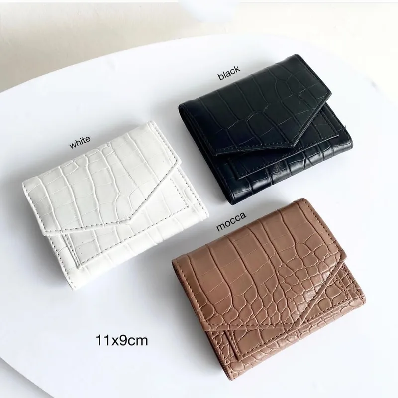 Tiga dompet lipat kecil bertekstur croco warna putih, hitam, dan mocca di atas meja putih dengan keterangan ukuran 11x9cm
