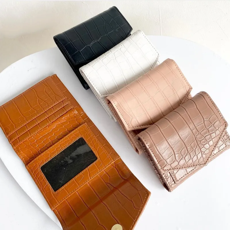 Dompet lipat bertekstur croco warna cokelat terbuka menampilkan slot kartu dan jendela kartu identitas, di sebelahnya empat dompet tertutup warna hitam, putih, pink, dan mocca