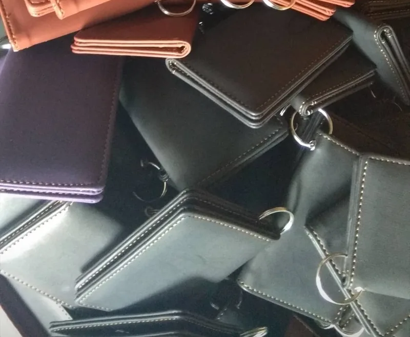Tumpukan dompet kunci lipat berwarna hitam, abu-abu tua, ungu, dan cokelat dengan ring logam di salah satu sudutnya