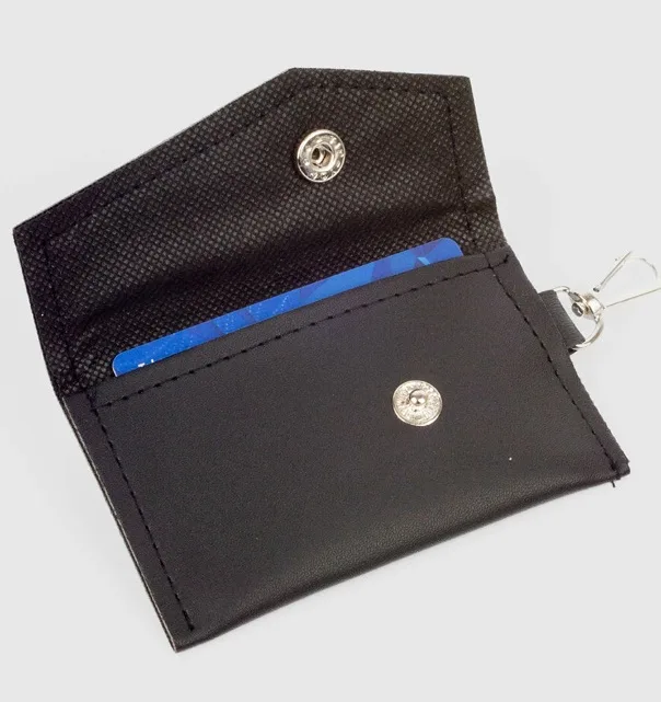 Gantungan kunci model dompet STNK hitam dalam posisi terbuka memperlihatkan kartu biru di dalam, dengan kancing logam dan cantolan besi di sudut kanan atas, di atas latar abu-abu muda