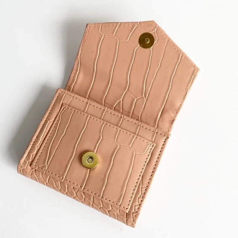 Dompet lipat kecil berwarna salem bertekstur motif buaya dalam keadaan terbuka, memperlihatkan dua kancing magnet bulat berwarna emas di penutup dan di badan dompet, di atas latar putih