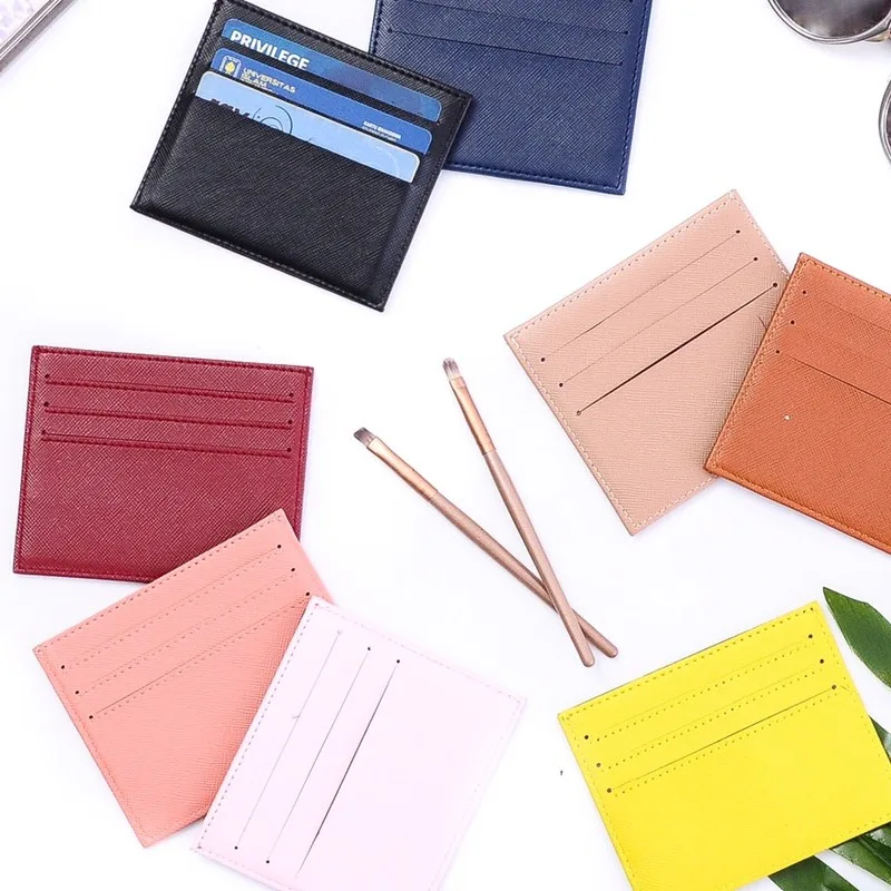 Delapan card holder tipis berwarna hitam, biru dongker, merah marun, salem, merah muda pucat, krem, cokelat jingga, dan kuning tersebar di atas meja putih