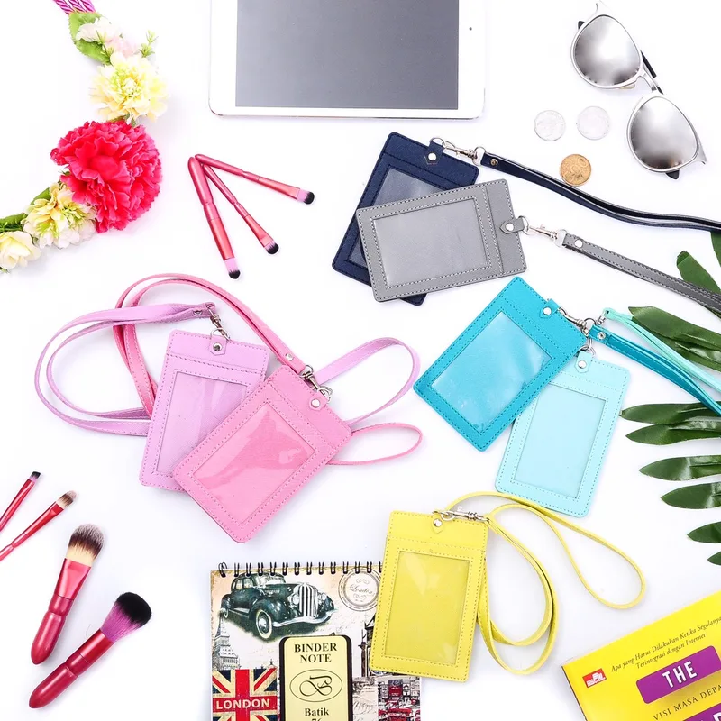Tujuh ID card holder bertali dalam warna biru dongker, abu-abu, ungu muda, merah muda, biru toska, biru muda, dan kuning tersusun di atas meja putih bersama bunga, kuas kosmetik, dan kacamata