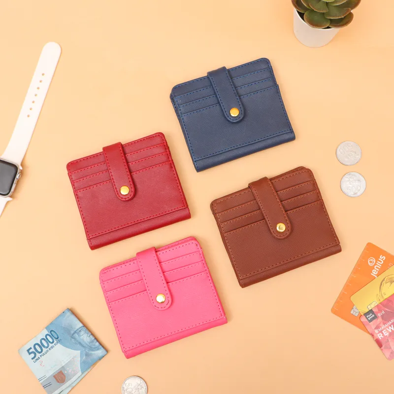 Lima dompet kartu kecil warna merah, biru dongker, merah muda, dan cokelat dengan kancing emas, di atas latar oranye muda bersama uang kertas dan koin