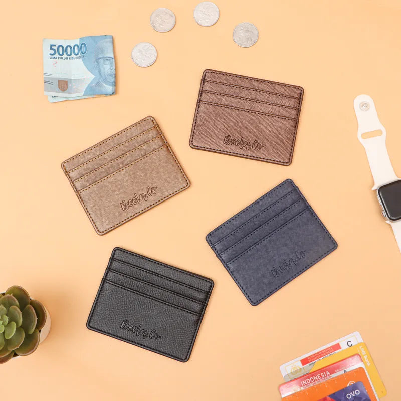 Empat card holder warna cokelat muda, cokelat tua, hitam, dan biru dongker dengan tulisan Beela.Co emboss, di atas latar oranye muda bersama uang kertas, koin, dan jam tangan