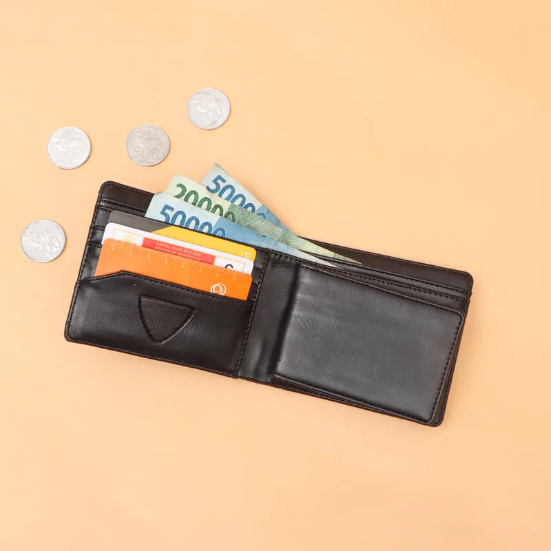 Dompet lipat hitam terbuka berisi kartu dan uang kertas di atas latar oranye muda, dengan beberapa koin di sekitarnya