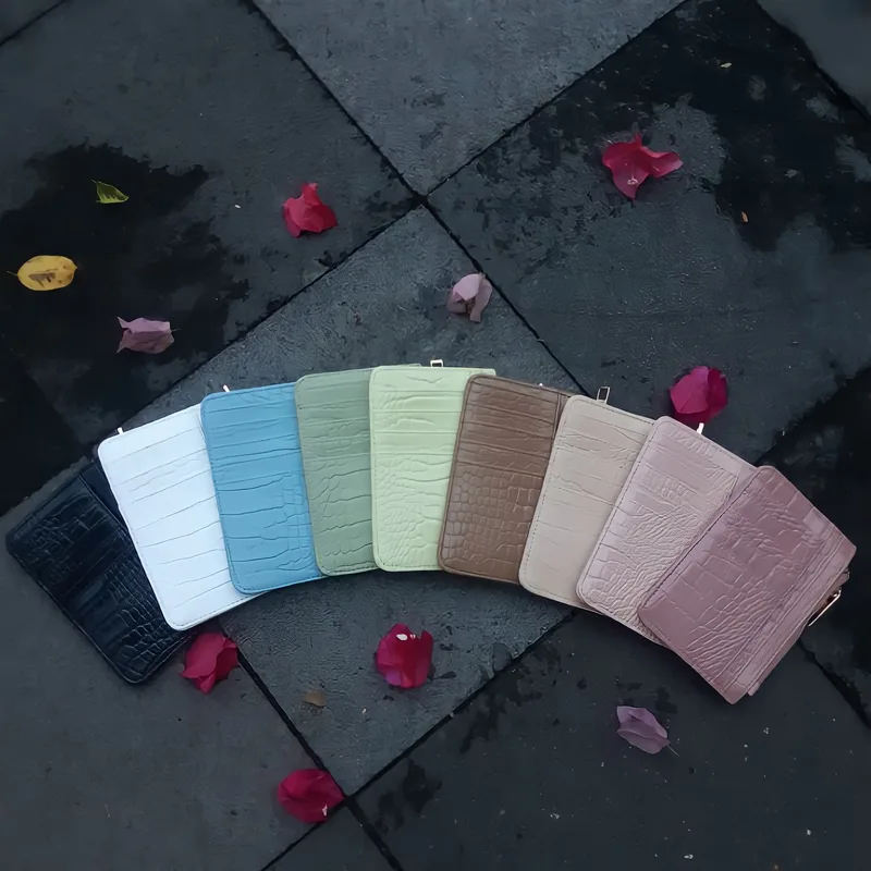 Deretan dompet kartu bertekstur croco dalam banyak warna, dari hitam, putih, biru muda, hijau mint, cokelat, krem, sampai merah muda, disusun di atas lantai batu gelap