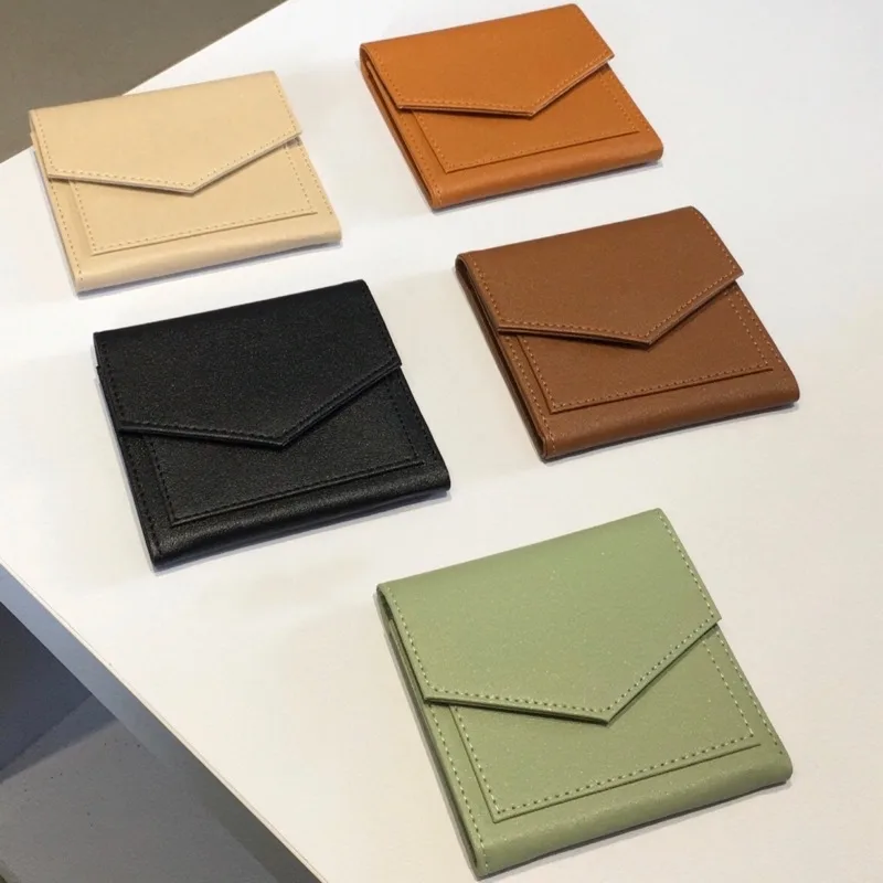 Lima dompet lipat bertutup amplop berwarna krem, cokelat, hitam, cokelat tua, dan hijau tersusun di atas meja putih