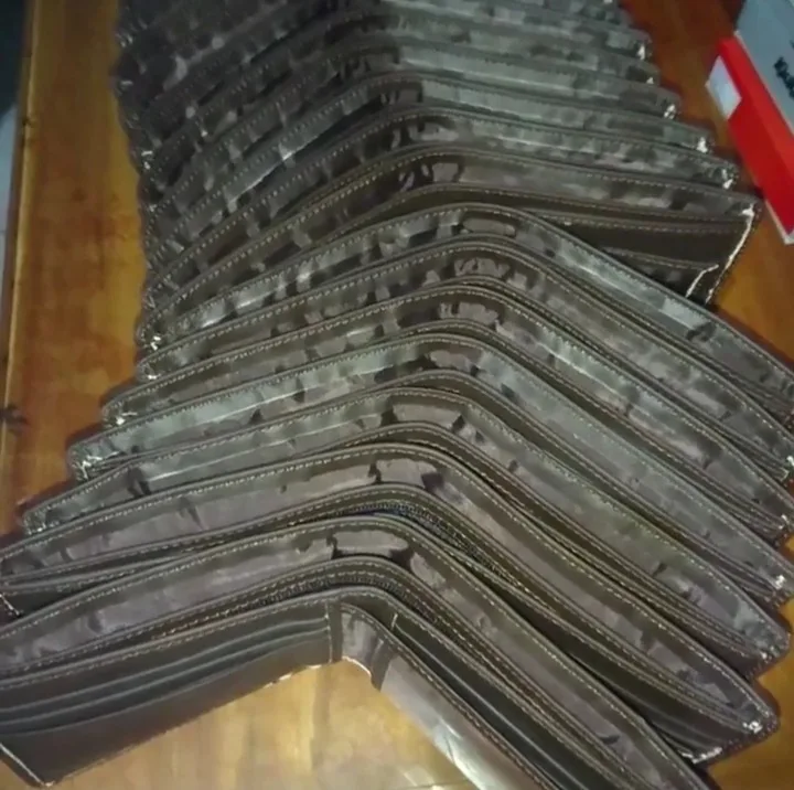 Dompet lipat warna abu-abu tua bertumpuk miring dalam barisan panjang di atas rak kayu