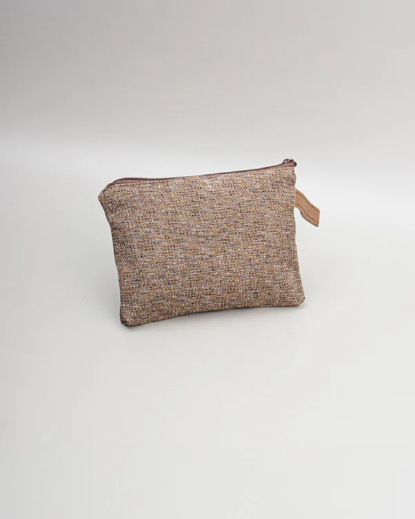 Pouch cokelat muda berbahan bertekstur seperti anyaman halus dengan ritsleting dan tarikan kecil berwarna krem, diletakkan di atas permukaan abu-abu muda