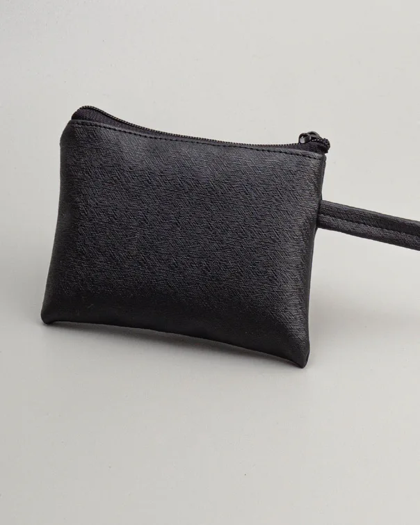 Pouch hitam polos bertekstur halus dengan ritsleting di bagian atas dan tali genggam yang memanjang ke kanan, difoto dari dekat di atas latar abu-abu muda