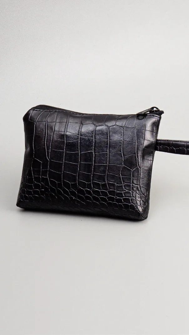 Pouch pipih hitam bertekstur croco dengan ritsleting di atas dan tali pegangan kecil di sisi kanan, di atas latar abu-abu