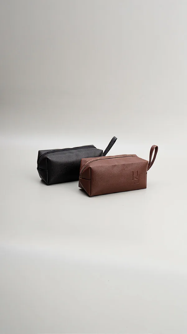 Dua pouch kubus kecil, satu hitam dan satu cokelat, masing-masing dengan tali pegangan kecil, di atas latar abu-abu