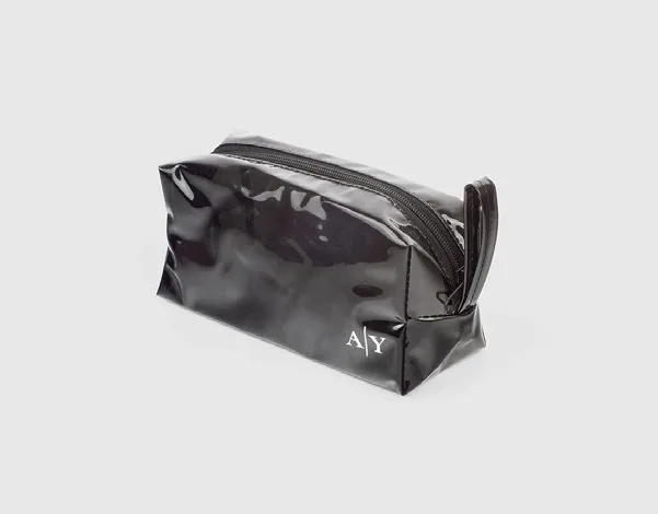 Pouch kubus hitam mengilap dengan ritsleting di atas dan tali kecil di sisi kanan, bertuliskan inisial A dan Y berwarna putih di sudut kanan bawah, di atas latar abu-abu muda