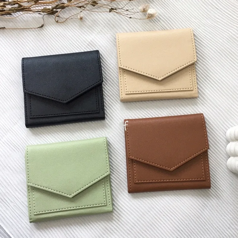Empat dompet lipat bertutup amplop berwarna hitam, krem, hijau mint, dan cokelat tertata dua baris di atas kain putih bergaris dengan ranting kering di bagian atas