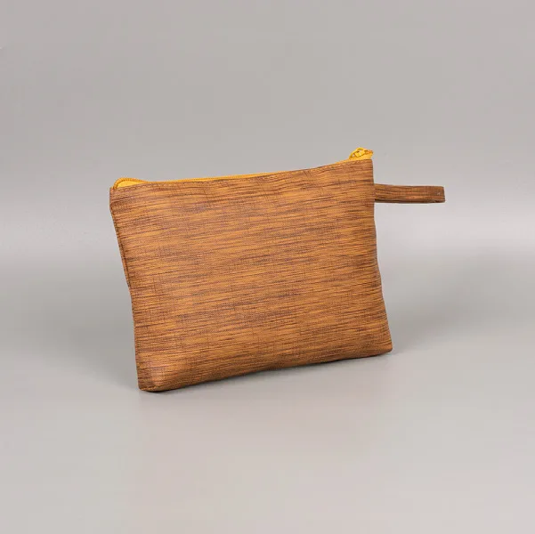 Pouch kapal berwarna cokelat keemasan bermotif serat kayu dengan ritsleting dan tali tangan pendek di atas latar abu-abu