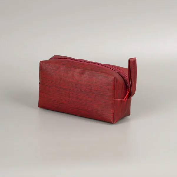 Pouch kubus berwarna merah marun dengan ritsleting dan tali kecil di sisi kanan, difoto miring di atas latar abu-abu