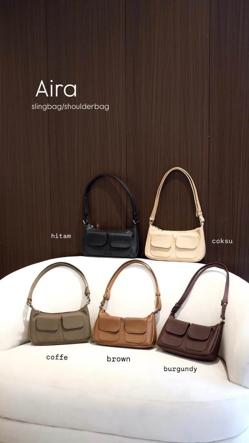 Lima tas selempang kulit warna hitam, krem, hijau olive, cokelat, dan marun tersusun di atas sofa putih dengan latar panel kayu