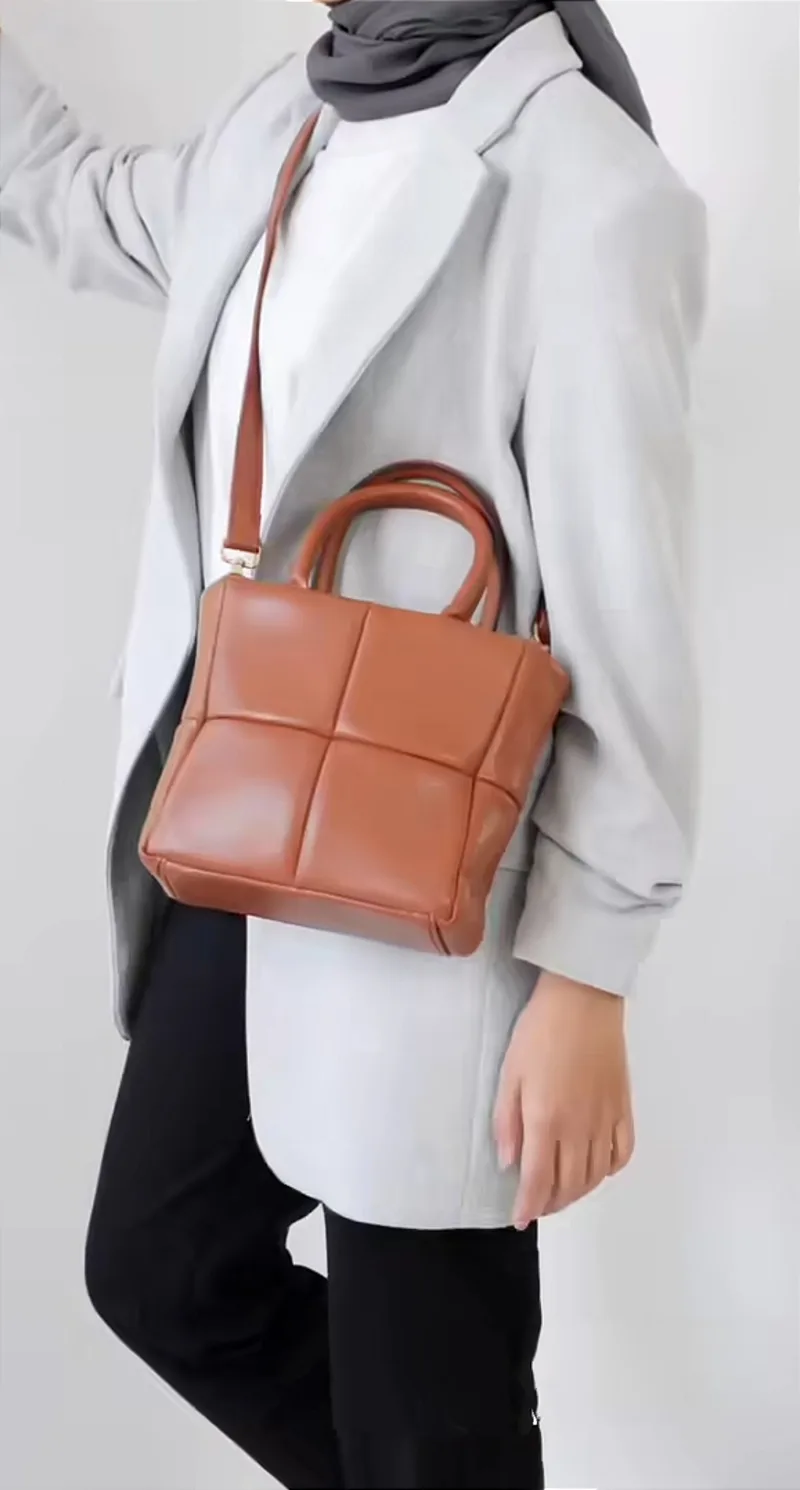 Tas tangan kotak berwarna cokelat dengan pola empat panel, dua pegangan bulat, dan tali selempang cokelat, dipakai di atas blazer abu-abu muda