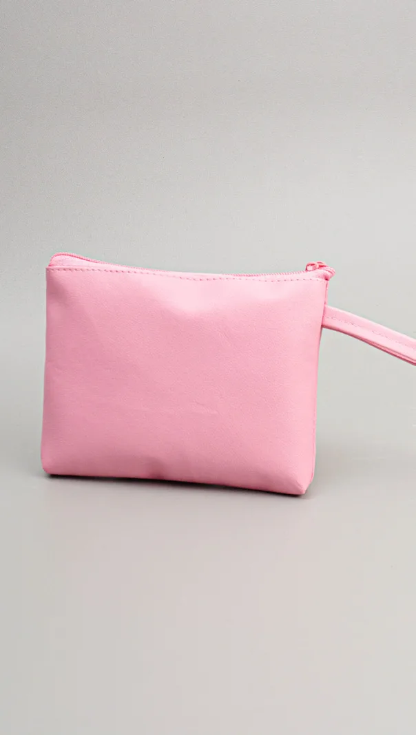Pouch berwarna pink muda polos dengan ritsleting di bagian atas dan tali genggam pink di sisi kanan, di atas latar abu-abu muda