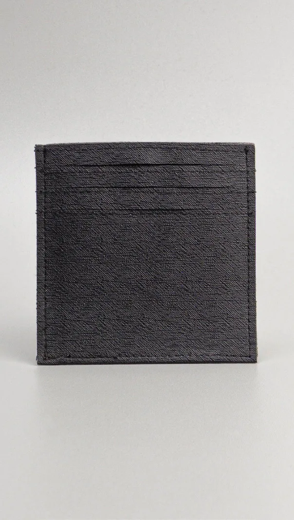 Card holder persegi berwarna hitam dengan permukaan bertekstur garis halus dan beberapa slot kartu di bagian atas, berdiri di latar abu-abu muda