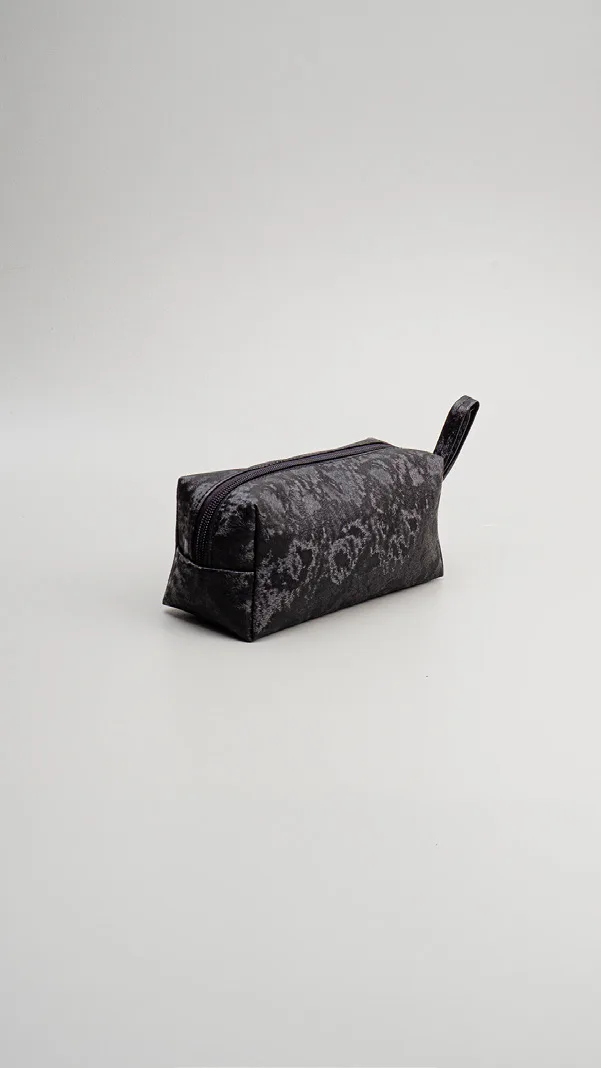 Pouch kubus hitam bermotif abu-abu samar seperti marmer dengan ritsleting di atas dan tali genggam pendek, diletakkan di latar abu-abu muda