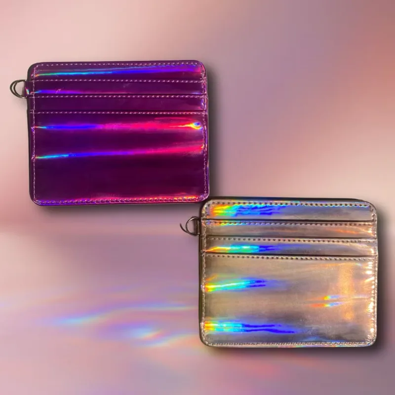 Dua card holder berpermukaan hologram, satu berwarna ungu magenta dan satu perak keemasan, masing-masing dengan cincin logam kecil di sudut, di atas latar merah muda berpendar