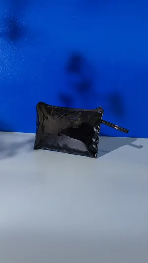 Pouch kapal hitam berbahan jelly mengilap dengan ritsleting dan tali tangan, berdiri di atas meja abu-abu dengan latar kain biru