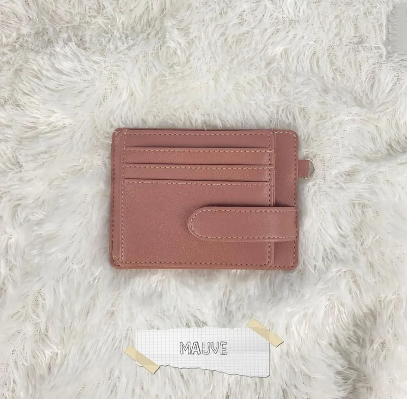 Card holder berwarna mauve dengan beberapa slot kartu bertingkat dan tali pengunci berkancing, diletakkan di atas karpet bulu putih dengan label kertas bertuliskan Mauve