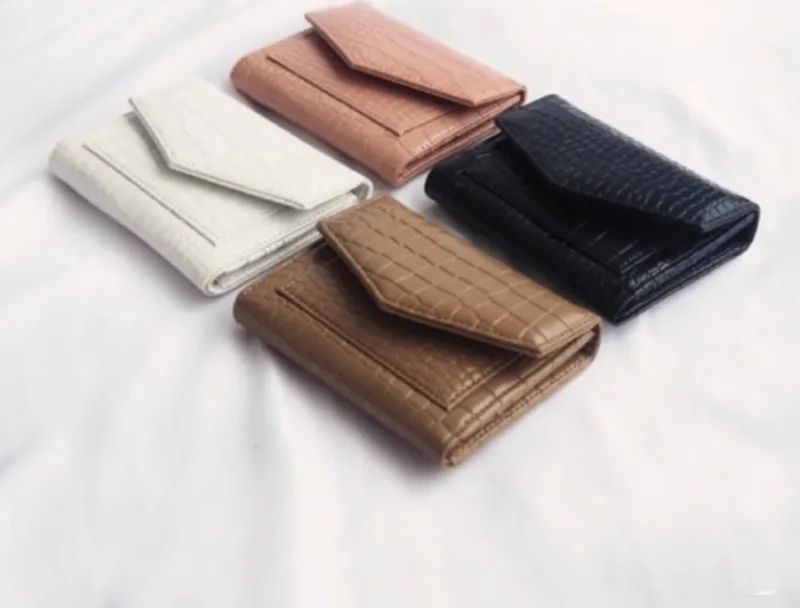 Empat dompet lipat kecil bertekstur motif croco berwarna putih, merah muda, cokelat susu, dan hitam dalam keadaan tertutup di atas kain putih