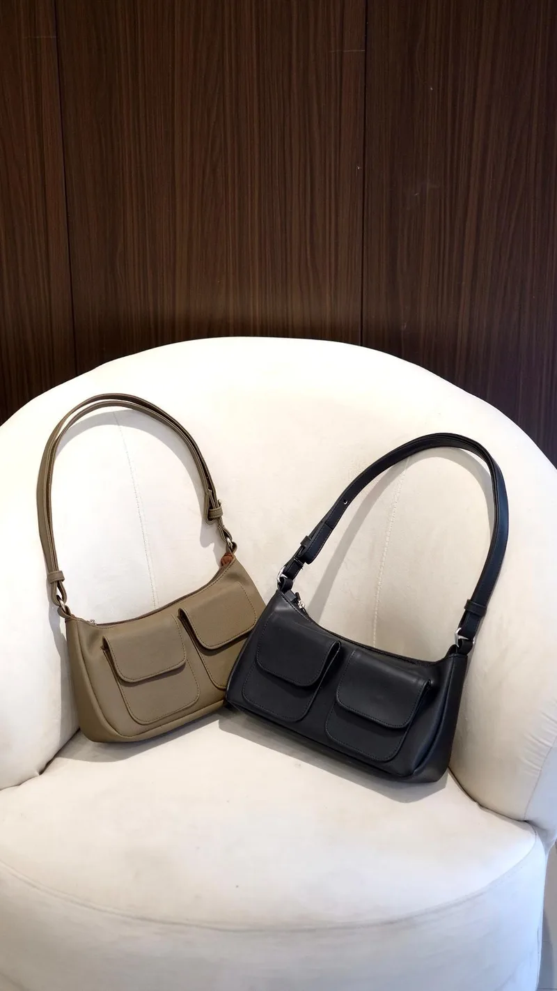 Dua shoulder bag berkantong ganda di bagian depan, satu warna cokelat keabuan dan satu hitam, diletakkan di kursi berlapis kain putih