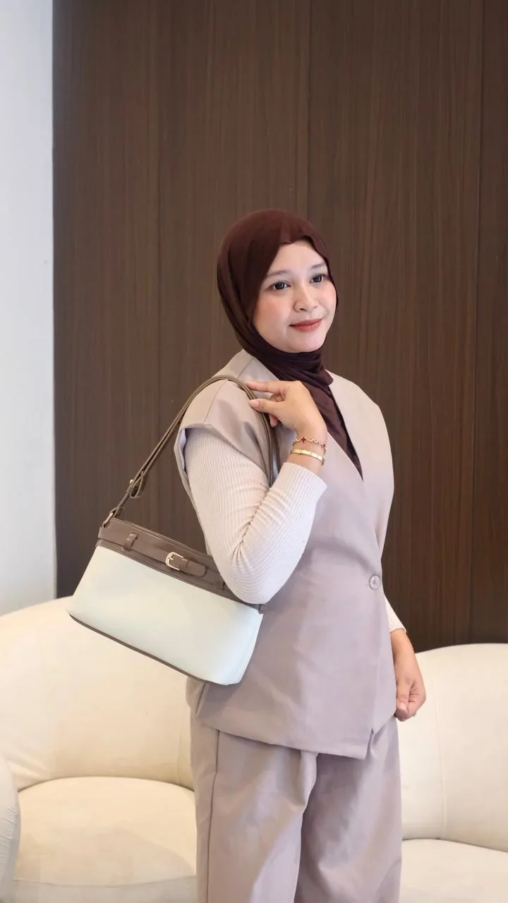 Perempuan berhijab cokelat dengan setelan rompi dan celana krem menyandang shoulder bag dua warna putih gading dan cokelat di bahu kiri