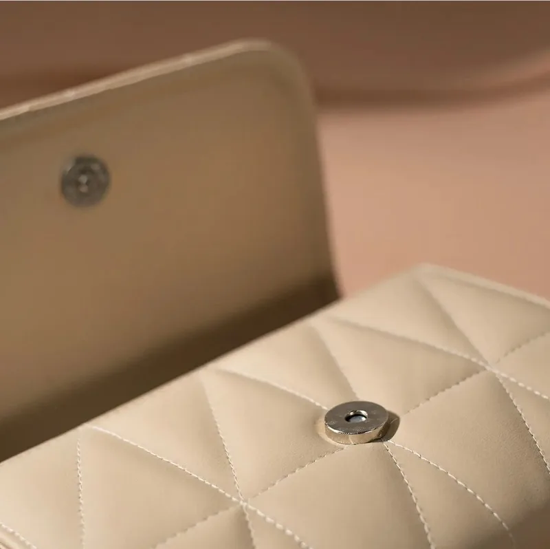 Close-up tutup tas krem bermotif quilting yang terbuka, memperlihatkan pasangan kancing magnet bulat berwarna perak