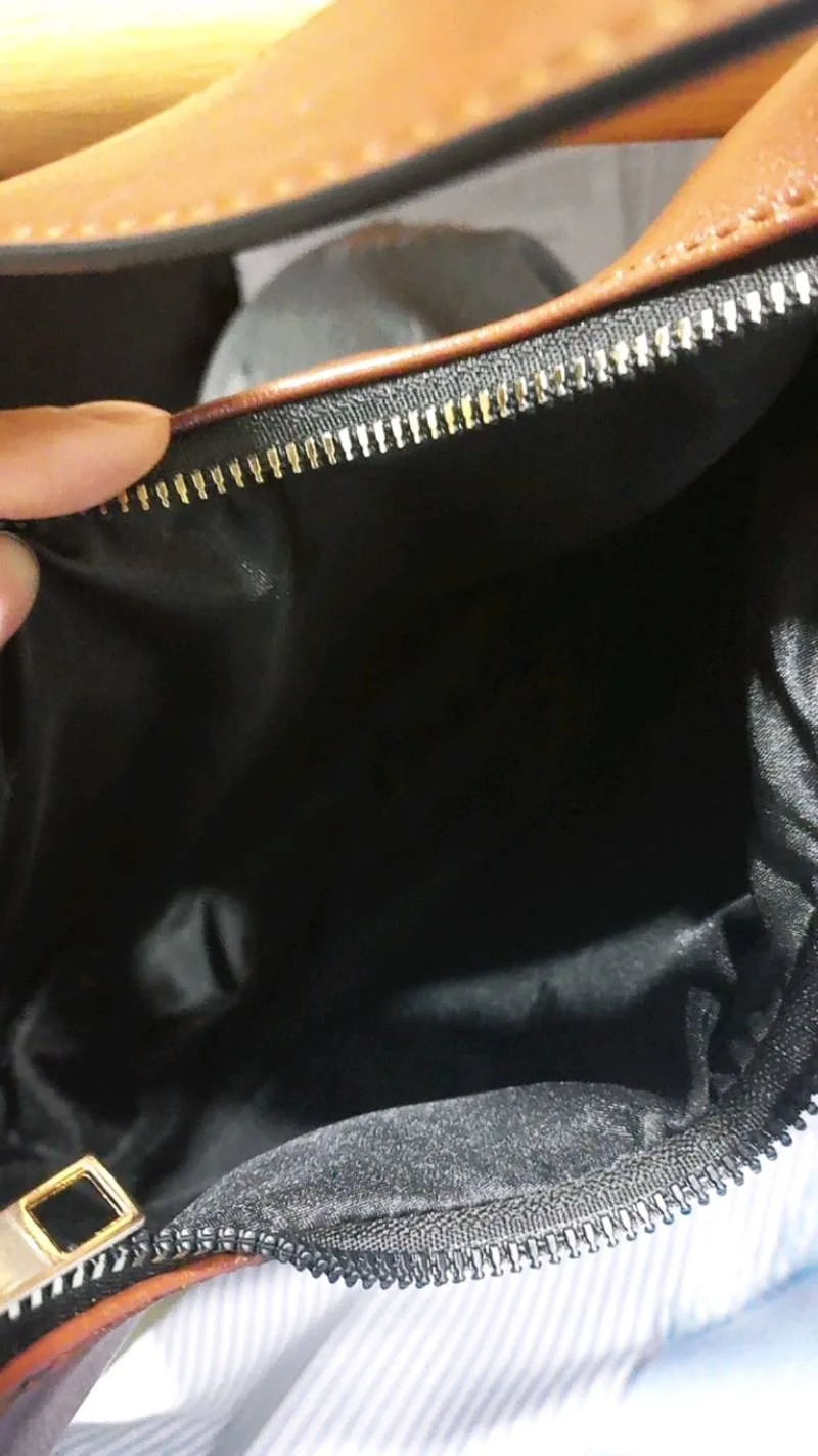 Bagian dalam tas yang dibuka memperlihatkan lapisan dalam berwarna hitam dan ritsleting logam, dengan tepi luar tas berwarna cokelat